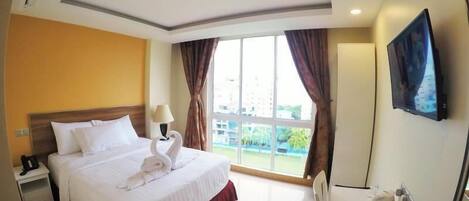 Quarto de hotel com cama, escrivaninha, cadeira, televisão e janela com cortinas.