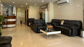 A modern hotel lobby with a reception desk, black leather sofas, a glass coffee table, and an air conditioning unit on the wall. - The Grand View (Malé)
