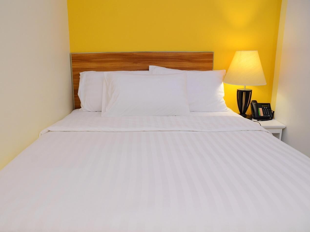 A neatly made bed with white linens and pillows, a wooden headboard, a bedside lamp, and a phone on a nightstand.