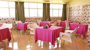 A dining area with tables covered in pink tablecloths, white chairs, and a tiled wall with a geometric pattern. - The Grand View (Malé)
