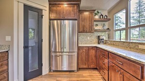 A kitchen with wooden cabinets, a stainless steel refrigerator, granite countertops, and a window overlooking a deck. - McCall Family Retreat | Pool, Hot Tub & Bikes (McCall)