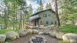 A cabin with a deck, surrounded by large rocks and a fire pit. - McCall Family Retreat | Pool, Hot Tub & Bikes (McCall)