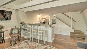 A spacious loft with a high ceiling, a kitchen area with bar stools, a staircase, and a dining area with a patterned rug. - Quaint Tignall Cabin w/ Deck & Private Dock! (Tignall)