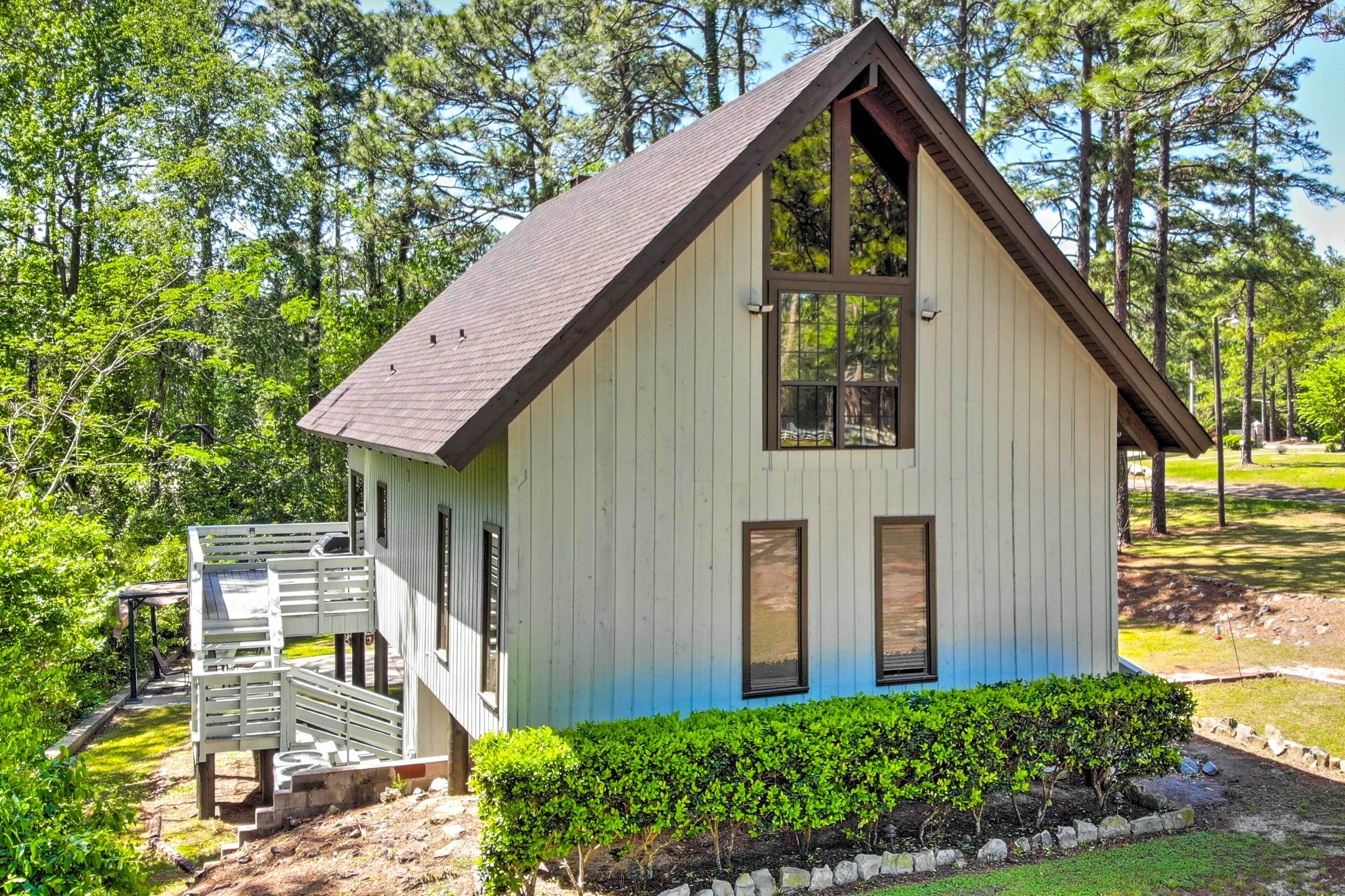 A small, single-story building with a sloped roof, a wooden deck, and a well-maintained hedge in front.
