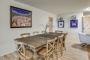 A dining area with a wooden table and chairs, a framed sports painting, and sports memorabilia on the wall.