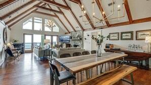 Un interior espacioso con techo alto, vigas de madera, una gran mesa de comedor y una zona de estar acogedora.