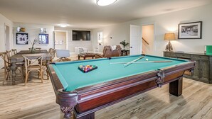Una mesa de billar con bolas, un comedor con sillas, un sofá y un televisor al fondo.
