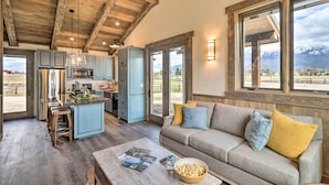 Un vaste espace de vie doté d’un plafond en bois, d’un canapé avec des coussins, d’une table basse avec des magazines et des collations, et offrant une vue sur les montagnes grâce à de grandes fenêtres.
