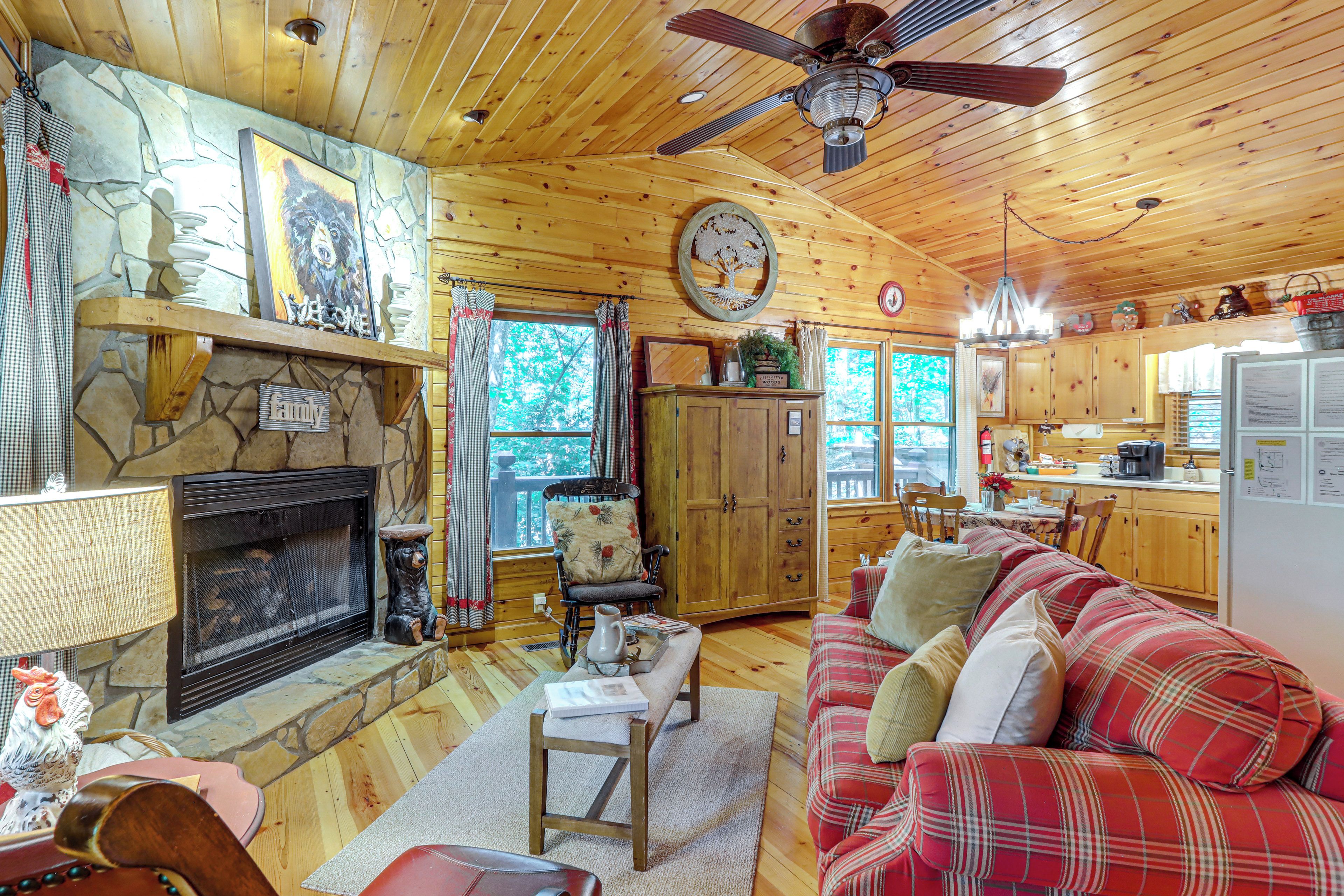 A cozy cabin interior with a fireplace, wooden furniture, and a kitchen area.
