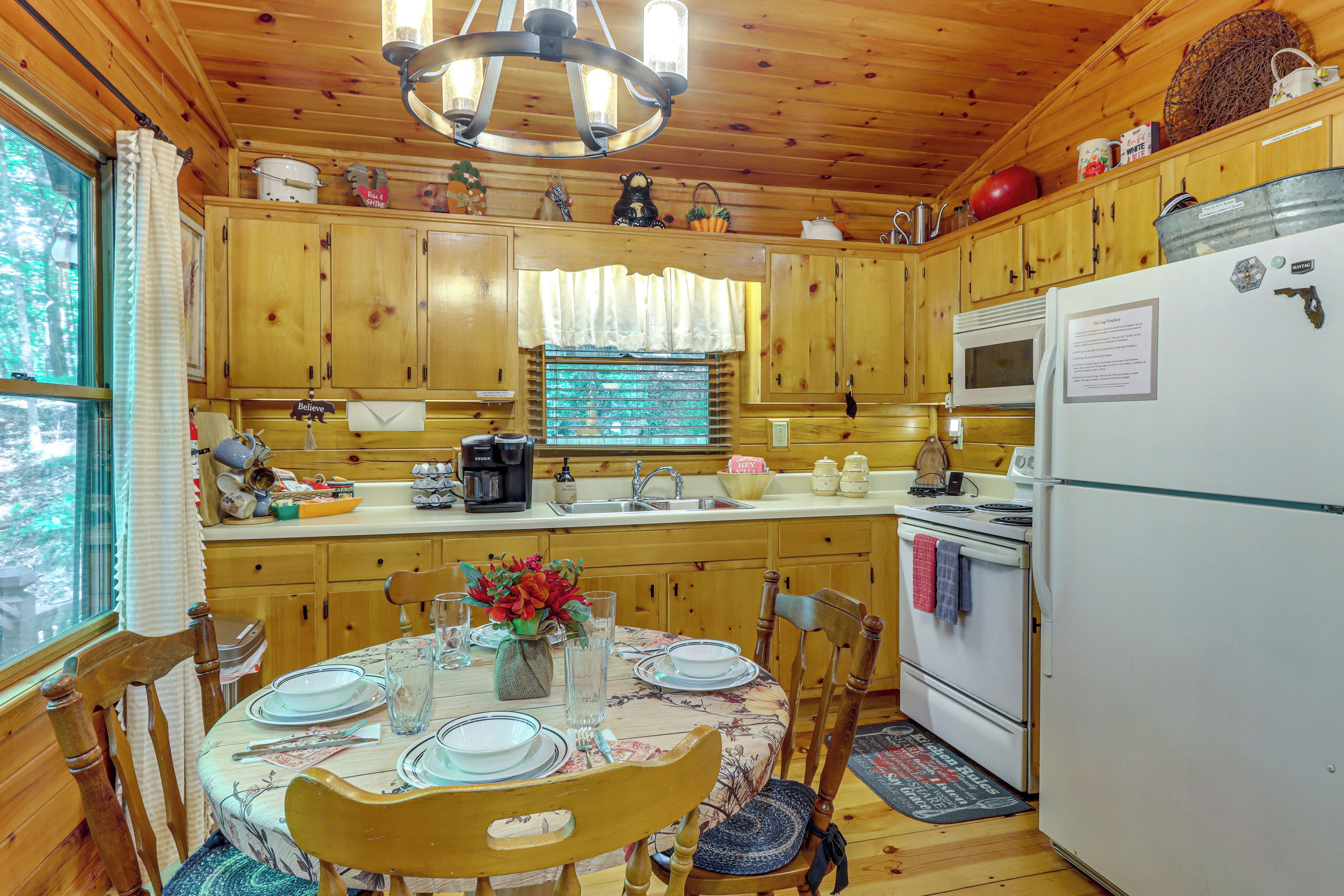 Une cuisine rustique aménagée dans une cabane en bois, avec une table à manger pour deux personnes, un réfrigérateur et une fenêtre avec des rideaux.