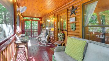 A wooden cabin with a porch, rocking chairs, a sofa, and a sign that reads 'Adventure Awaits'.