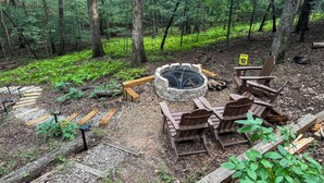 Ein Waldcampingplatz mit Feuerstelle, Holzhöcken und einem Schild mit Warnung vor Waldbränden.