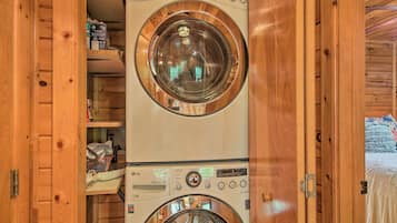 Un appareil combiné lave-linge et sèche-linge, de type «
empilable
», installé dans une cabane en bois, avec une étagère visible au-dessus du sèche-linge.