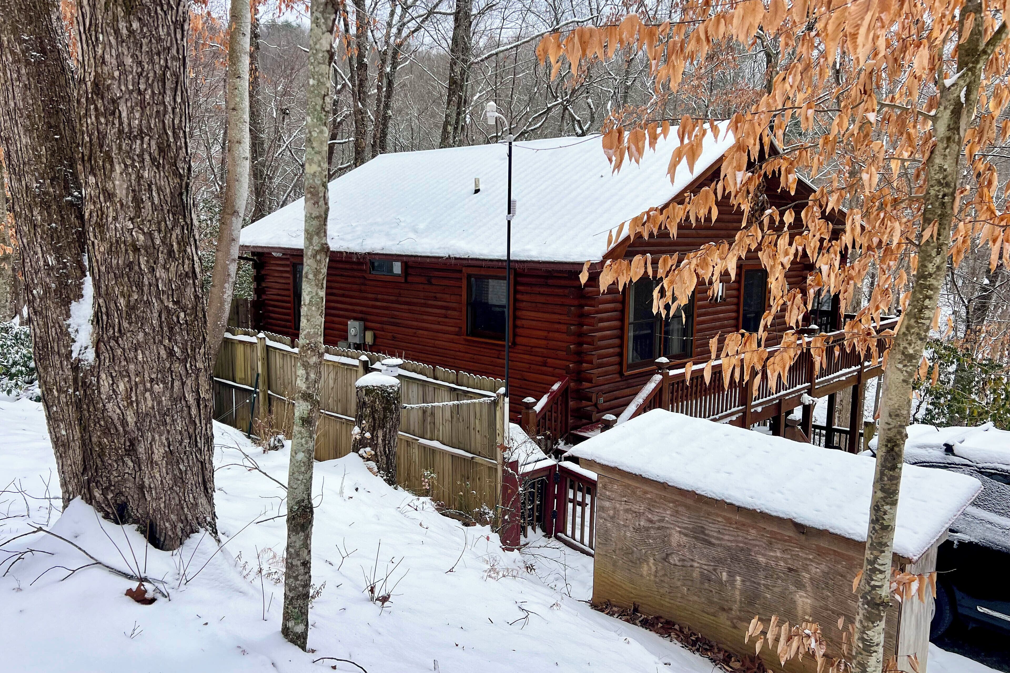 Une cabane en bois, dont le toit est recouvert de neige, entourée d’arbres et d’une clôture en bois.
