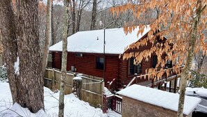 Eine Holzhütte mit schneebedecktem Dach, umgeben von Bäumen und einem Holzzaun.