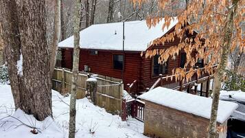 Une cabane en bois, dont le toit est recouvert de neige, entourée d’arbres et d’une clôture en bois.