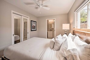 Een slaapkamer met een groot bed, een plafondventilator, een raam met uitzicht en een badkamer die door een open deur zichtbaar is.