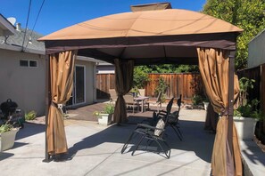 Een overdekt terras met een pergola, tuinmeubilair en potplanten.