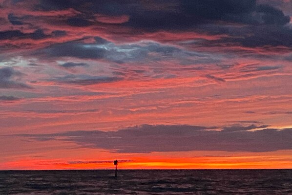 Un coucher de soleil sur l’océan, avec la silhouette d’une construction visible au loin.