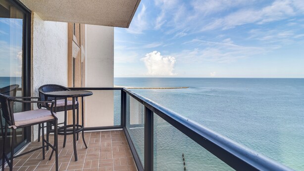 A balcony with a view of the sea, a table, and two chairs. - Dolphin & Manatee Viewing From 15th Floor (Clearwater)