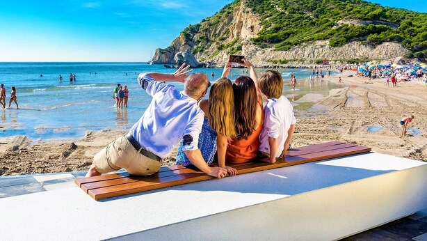 A beach with a wooden bench, people relaxing, and a hill in the background.