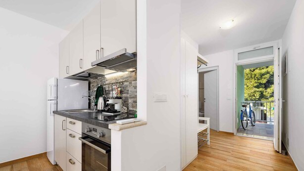 A compact kitchen with white cabinets, a stove, and a sink. A bicycle is visible through an open door leading to a balcony. - Holiday apartment near the beach and with air conditioning (Umag)