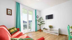 A living room with a red sofa, a potted plant, a TV mounted on the wall, and a sliding glass door leading to a balcony. - Holiday apartment near the beach and with air conditioning (Umag)