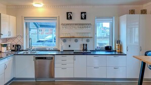 Une cuisine moderne avec des meubles blancs, un lave-vaisselle en acier inoxydable et une fenêtre donnant sur la rue.