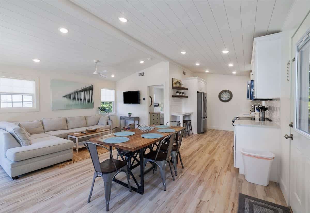 A modern kitchen with white cabinets, a dining table with chairs, a sofa, and a TV.