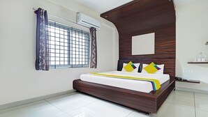 A bedroom with a bed, window with curtains, air conditioning unit, wooden headboard, bedside table, and a wall-mounted shelf. - Itsy Hotels Colors Stay (Chikkamagaluru)
