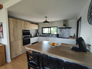 A modern kitchen with wooden cabinets, a central island with chairs, and a black coffee machine.