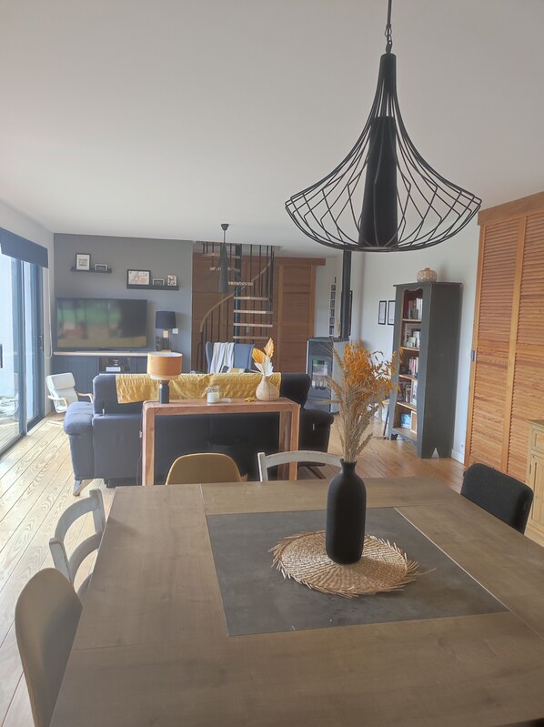 A modern living room with a dining area, featuring a large TV, comfortable seating, and a unique pendant light.