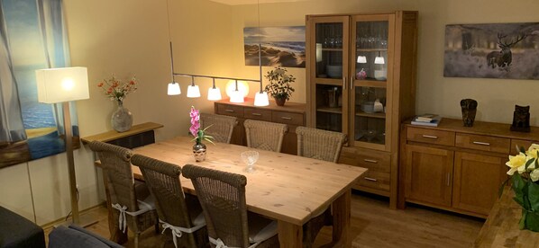 A dining area with a wooden table and wicker chairs, a cabinet with glass doors, and a painting on the wall.