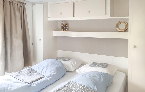 A bedroom with two beds, a wardrobe, and a shelf with a clock and a decorative item. - 2 bedroom lovely home in Renesse (Renesse)