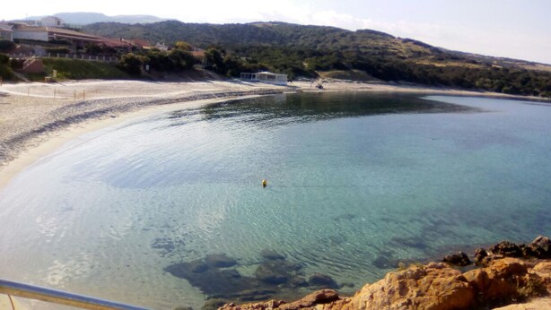 A coastal view with clear water, a sandy beach, and a rocky shoreline.