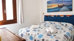 A bedroom with a bed, a window, a painting, and a wooden headboard.