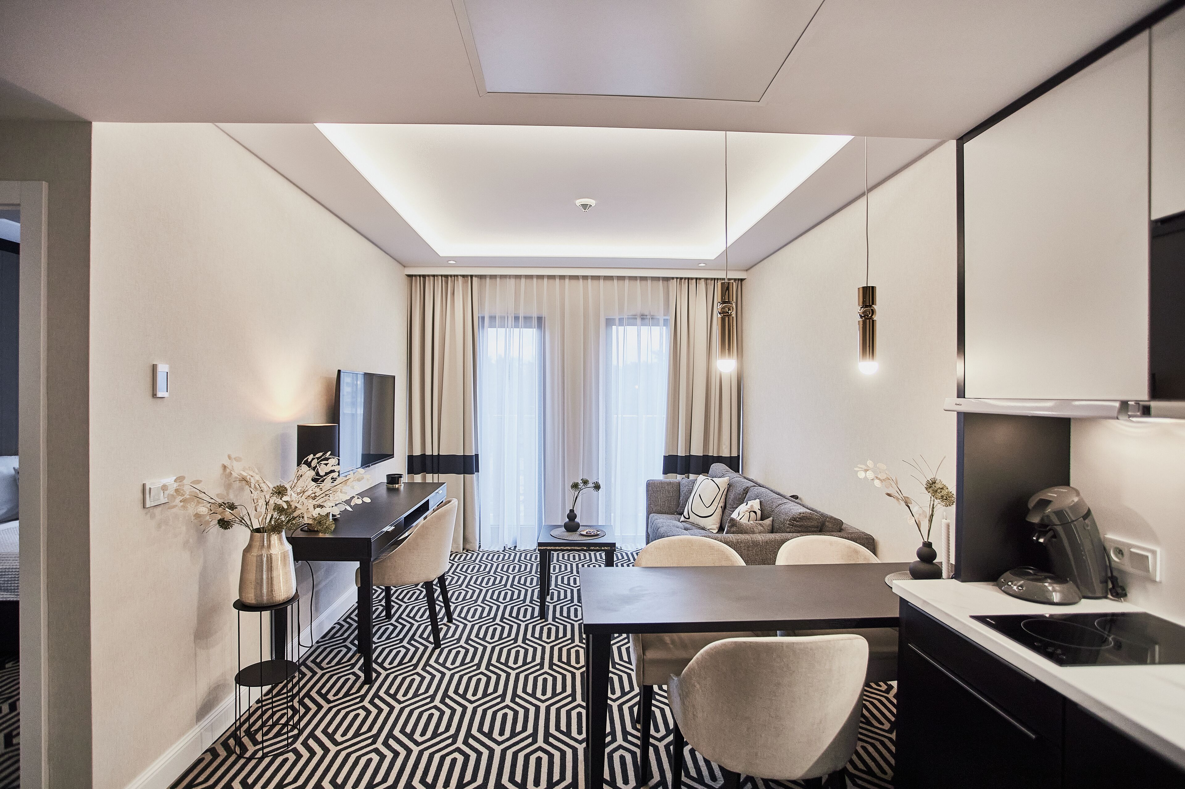 A modern hotel room with a dining area, a sofa, a TV, and a kitchen area.