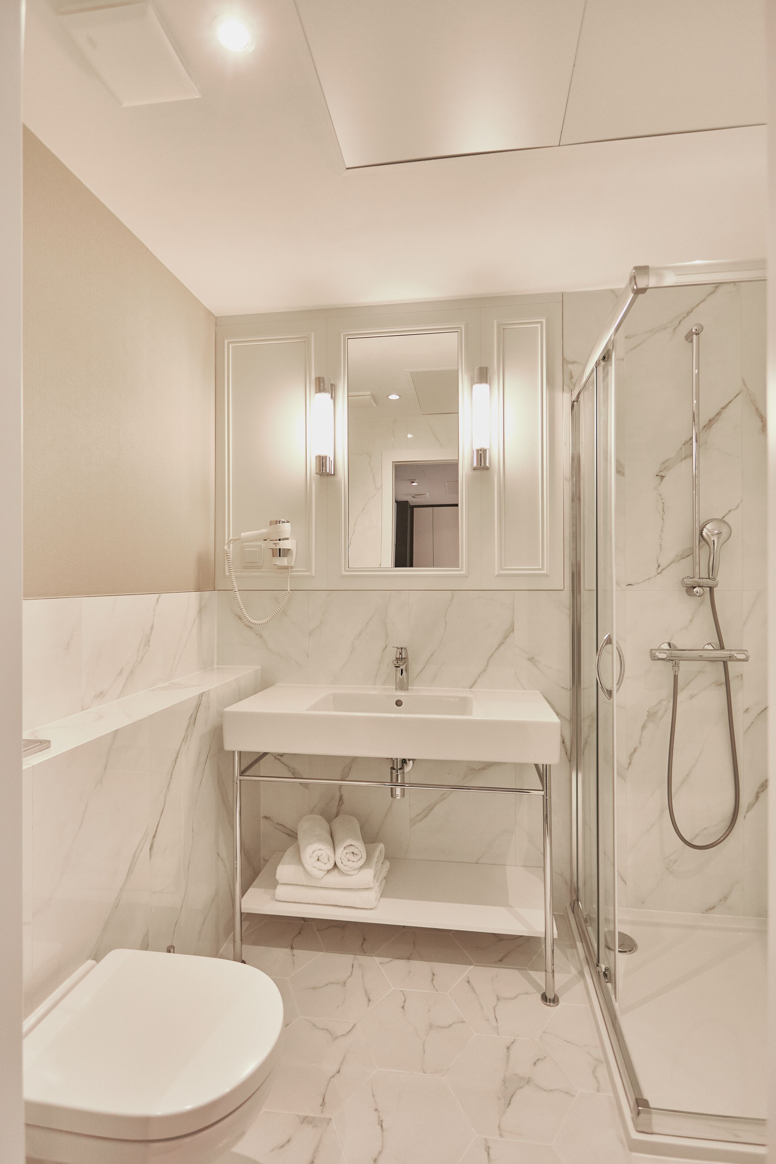 A modern bathroom with a marble sink, a glass-enclosed shower, and a toilet.