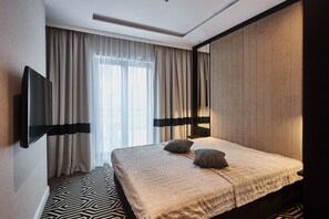 A hotel room with a bed, curtains, a flat-screen TV, and a patterned floor.