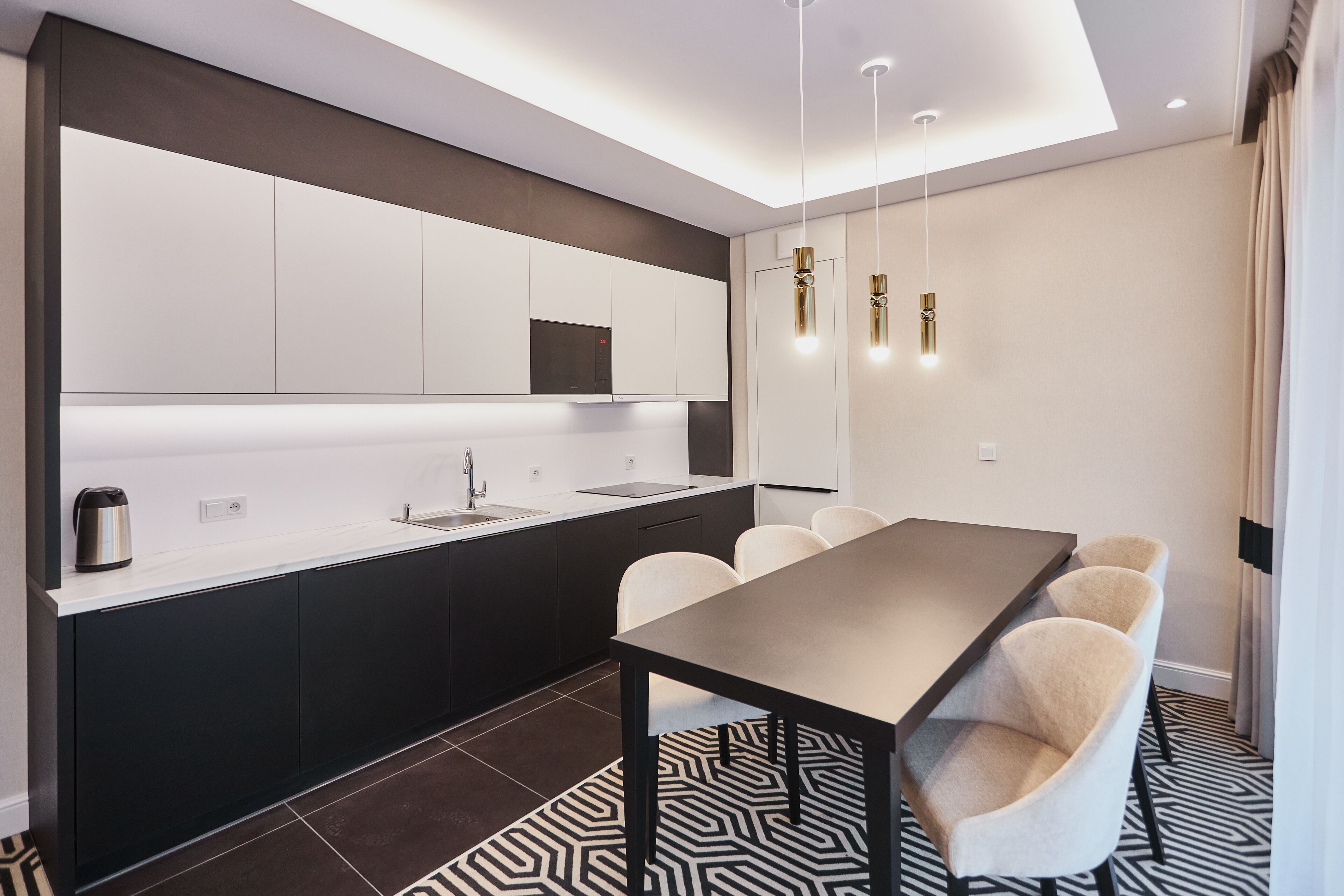 Une cuisine moderne avec un coin repas, comprenant une longue table et des chaises, un four encastré et un éclairage suspendu.