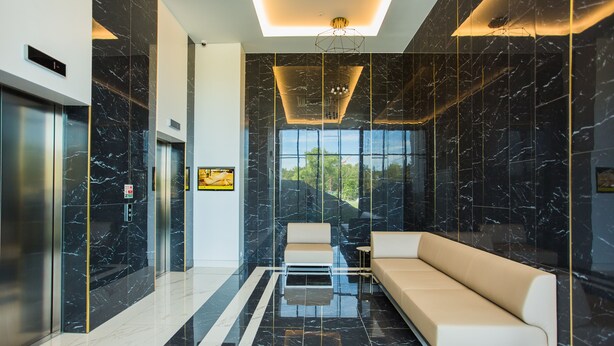A modern lobby with a black marble wall, a glass coffee table, a beige sofa, and a large window offering a view of greenery. - Apartamenty Świnoujście - Uzdrowiskowa 40G (Swinoujscie)