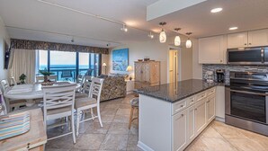Een moderne keuken met een groot eiland, roestvrijstalen apparatuur en uitzicht naar buiten.