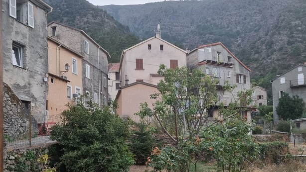 A rustic village with stone buildings, a small garden, and a mountainous backdrop.