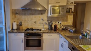 A kitchen with white cabinets, a stainless steel range hood, a microwave, and a sink.
