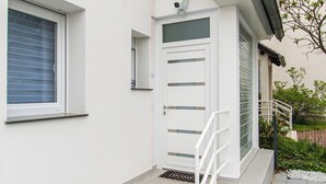 Un edificio blanco con puerta principal, una ventana pequeña y una cámara de seguridad.