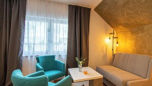 Una habitación con un sillón azul verdoso, un sofá color crema, una mesita blanca y un jarrón con flores.