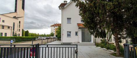 A gated pedestrian walkway leading to a white building with a small entrance and a visible window.