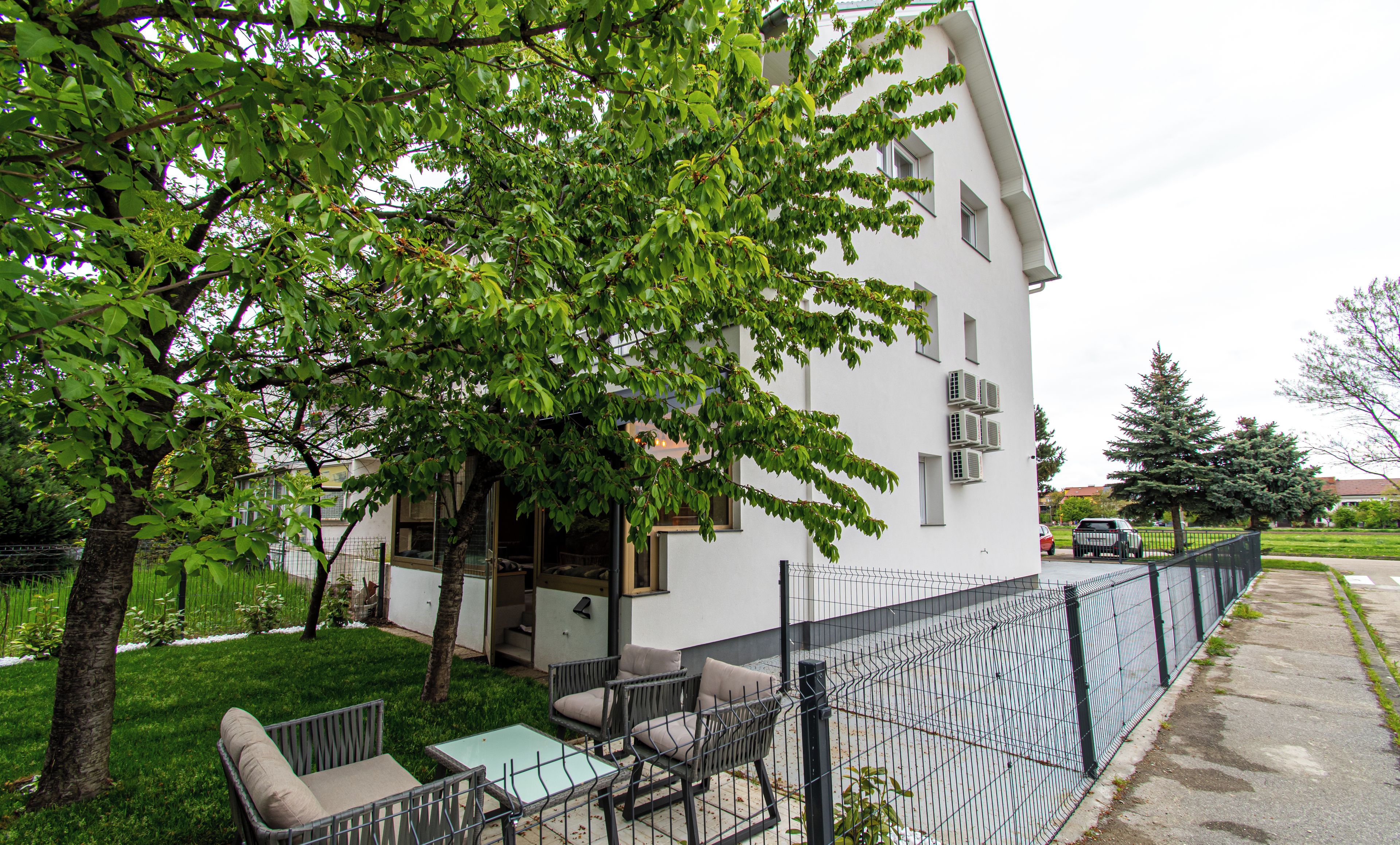 Un edificio residencial con un patio cercado, mobiliario exterior y un árbol que da sombra.