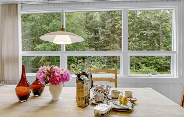 Enjoy a peaceful retreat with a forest view, featuring a table set with a teapot, cups, and utensils, and a vase with fresh flowers.