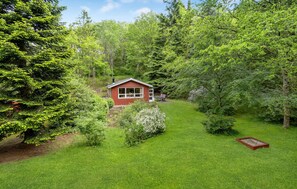 Escape to a serene cabin nestled in a lush forest, surrounded by a well-maintained lawn and shrubs.